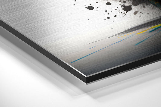 Close-up angled view of brushed aluminum Dibond panel showing white surface with black ink splatters and colored lines.