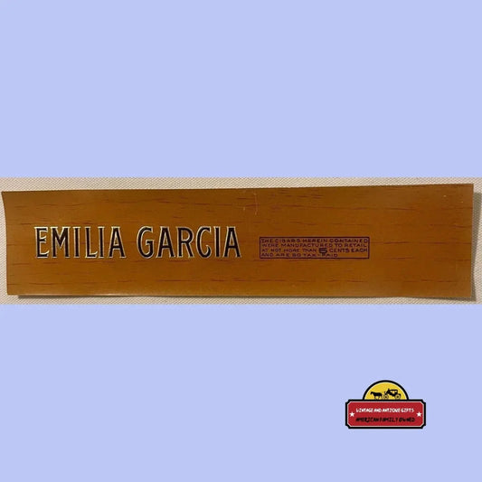 Tan wooden cigar box label reading "Emilia Garcia" with embossed silver letters and tax stamp.