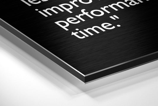 Close-up angled view of layered brushed aluminum and white composite panel with white printed text about performance and time.