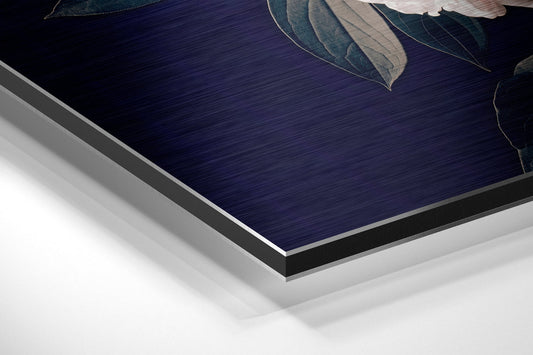 Angled close-up view of layered brushed aluminum dibond showing dark navy surface with white border edge and decorative leaves visible at top.