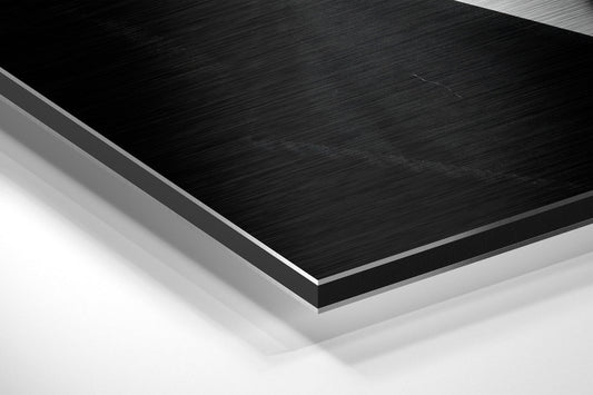 Close-up angled view of layered composite material showing black brushed aluminum surface with white and gray backing layers.