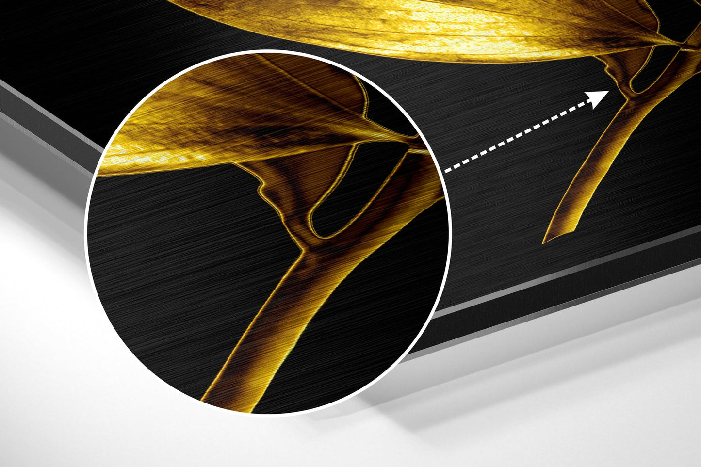 Close-up detail of golden leaf veins against black brushed aluminium surface with magnifying circle highlight and directional arrow.