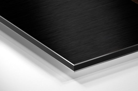 Close-up detail shot showing layered edge of black brushed aluminum dibond panel with silver beveled trim against white background.