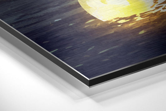 Close-up angled view of layered wall art showing brushed aluminum dibond panel with dark ocean and golden moon detail.