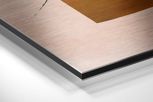 Close-up angled view of layered Dibond composite material showing brushed aluminum surface with black edge banding and wooden backing.