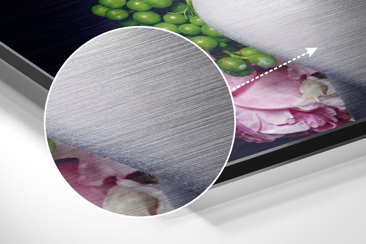 Close-up detail of brushed aluminium surface texture with pink flowers and green foliage visible at edges.