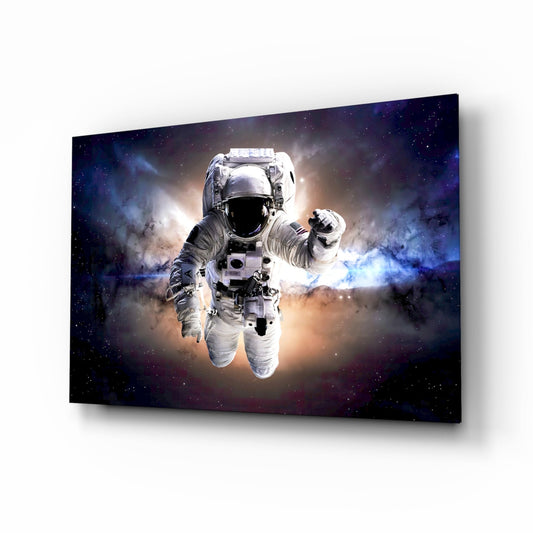 Angled perspective of glass wall art displaying a white spacesuit astronaut floating against a cosmic nebula background with blue, purple, and golden light effects.