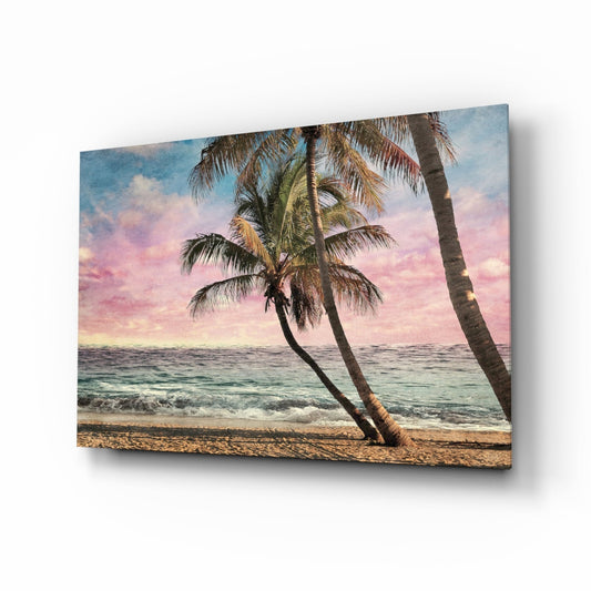 Glass wall art canvas displaying a tropical beach scene with leaning palm trees, pink sunset sky, and turquoise ocean waves.
