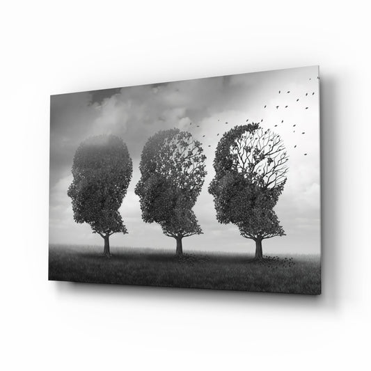 Three human head-shaped trees in profile view progressively losing foliage and leaves, rendered in black and white on glass wall art displayed at an angle.