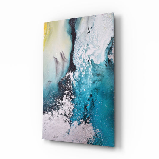 Angled side view of a glass wall art panel displaying aerial coastal imagery with teal, white, and yellow pigments swirling together.