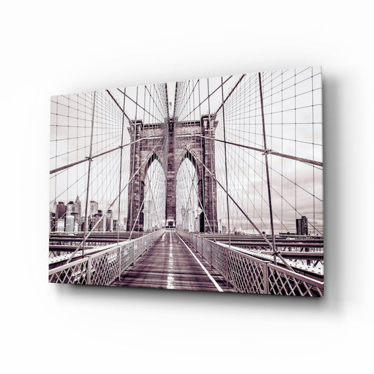 Symmetrical view down Brooklyn Bridge's wooden walkway with steel cable railings and Manhattan skyline in muted purple tones.