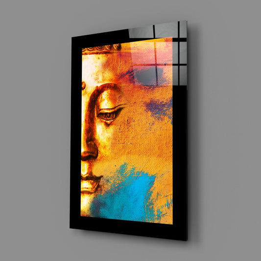 Black-framed glass wall art displaying a Buddha profile in gold, orange, and blue tones, photographed at an angle against gray background.