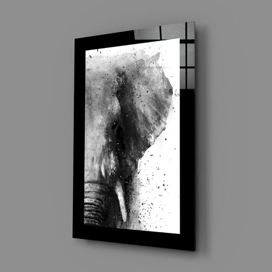Black-framed glass wall art displaying a monochromatic elephant head with watercolor splatter effect, mounted at an angle against gray wall.