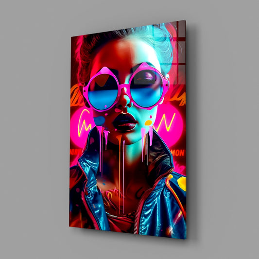 Angled view of glass wall art featuring a neon-styled portrait of a woman wearing oversized pink round sunglasses with cyan-blue lenses, vibrant magenta and cyan lighting effects, and dripping paint details on dark background.