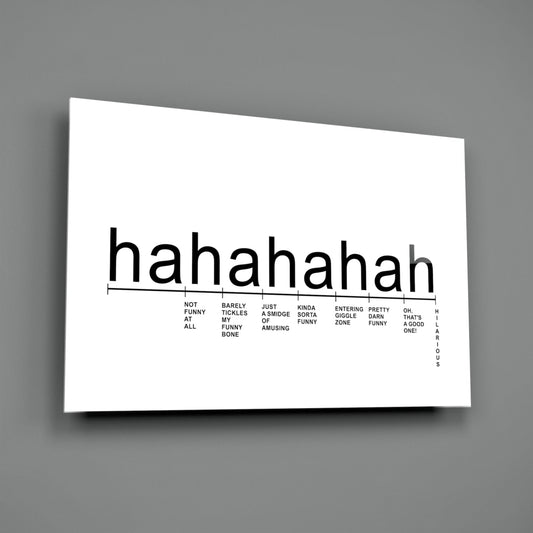 White glass wall art panel mounted on gray wall displaying "hahahah" text with humorous laughter intensity scale below.