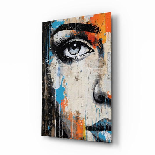 Glass wall art panel displaying a stylized half-face portrait with bold black eye and lips, vibrant orange and blue paint splatters on cream background, angled three-quarter view.