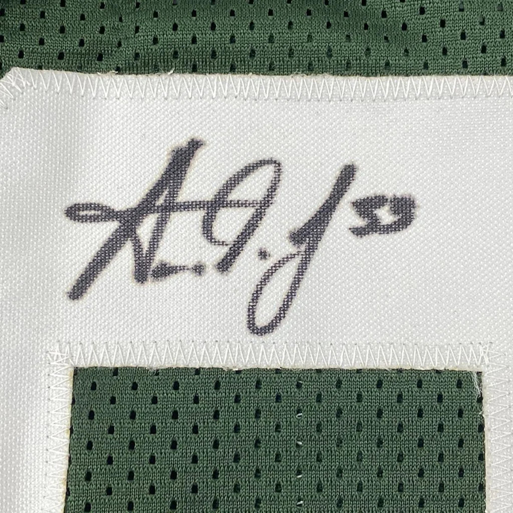 Black cursive a.g.j. stitched signature on white label bordered by green mesh on framed signed green bay jersey