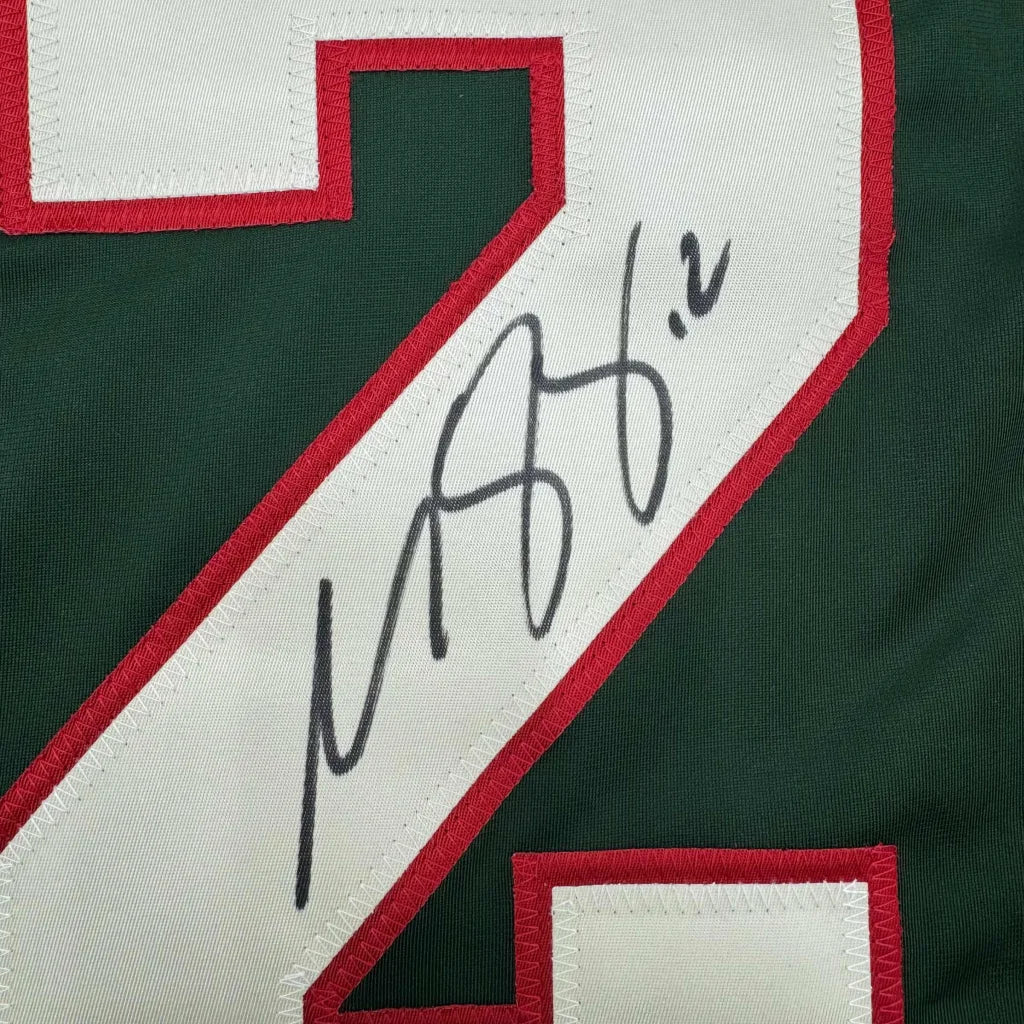 Autographed green and white Minnesota Wild jersey with red trim in a frame with photos