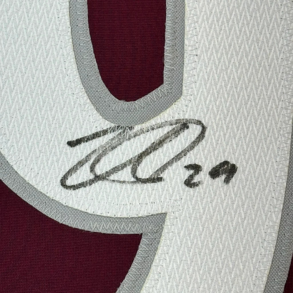 A close-up of a white and maroon colorado hockey jersey with gray trim and an embroidered black signature