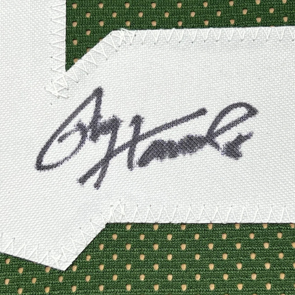 A black ink ogorman signature stitched on white fabric patch bordered by green mesh on a framed signed green bay jersey