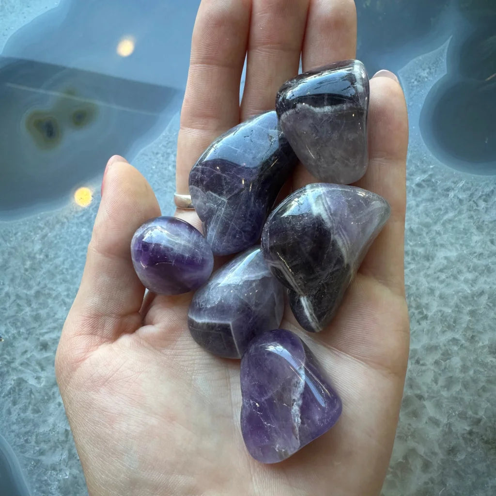 Hand holding large tumbled amethyst stones in purple shades for crafts