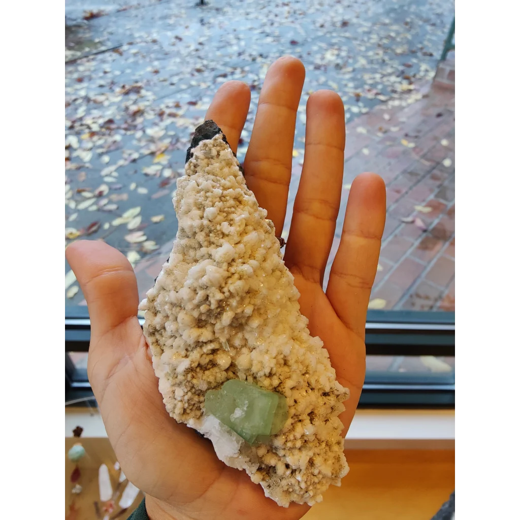 Green apophyllite with mordenite: hand holding green fluorite in calcite matrix