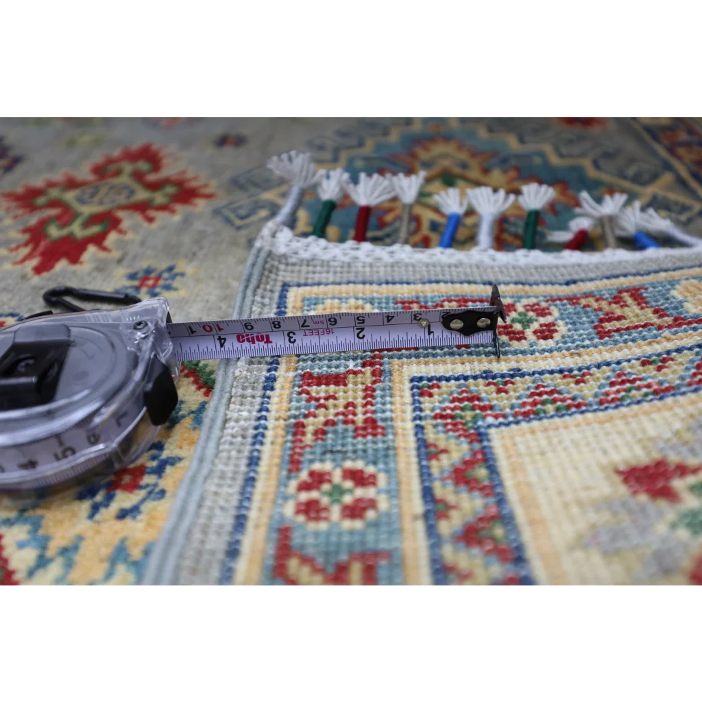 Silver tape measure on hand-knotted Afghan Kazak wool rug with cotton foundation