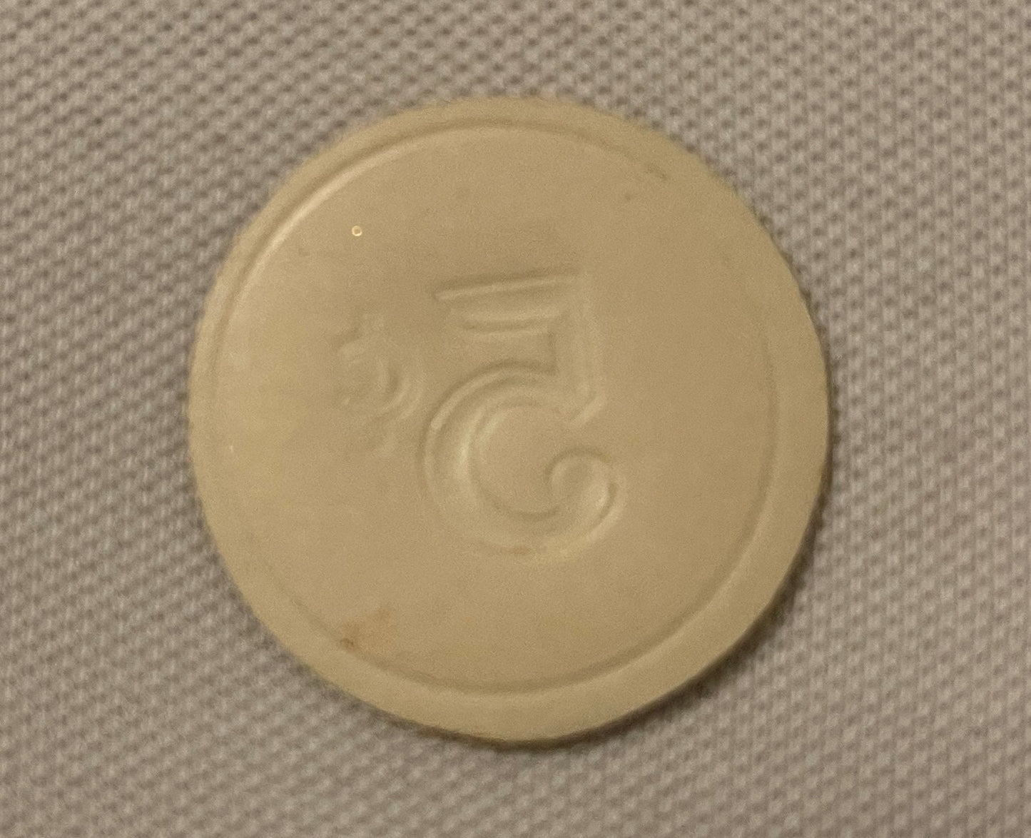 Cream-colored round embossed token with number 5 and decorative scrollwork, photographed flat on textured fabric background