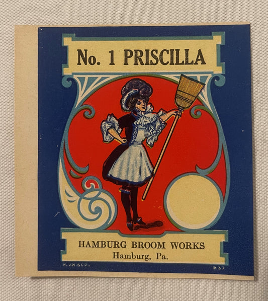 Vintage broom label featuring an Art Nouveau design with a woman holding a broom against a red circle, navy border, and cream