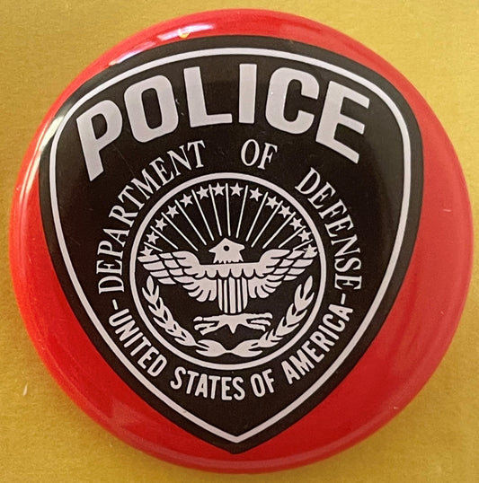 Circular red and black tin litho badge with white eagle seal and "POLICE - DEPARTMENT OF DEFENSE - UNITED STATES OF AMERICA"