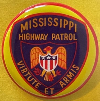 Circular tin litho police badge with yellow border, dark blue center featuring gold eagle, red and white shield, and text "Mi