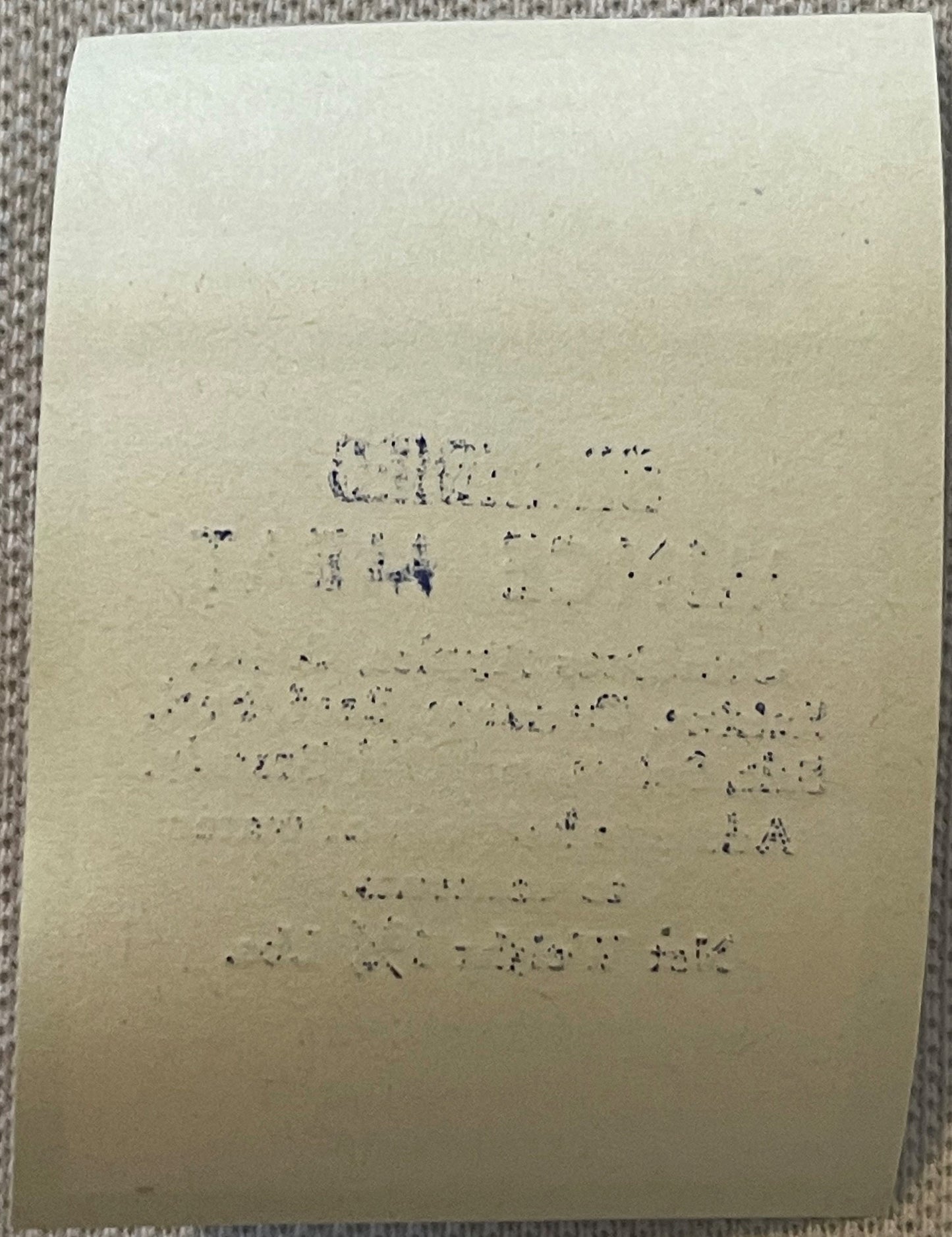 Aged cream-colored label with faded typewritten text, photographed flat against gray textured fabric background
