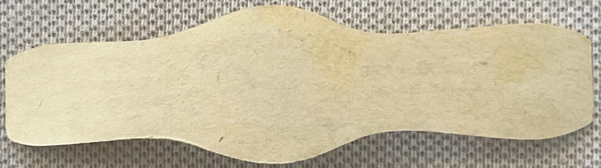 Cream-colored scalloped cigar band with wavy edges on textured gray fabric background