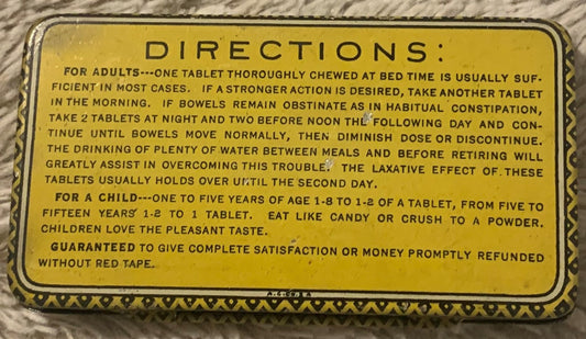 Vintage Pinex Laxatives tin with yellow label showing dosage directions for adults and children, laid flat on textured fabric