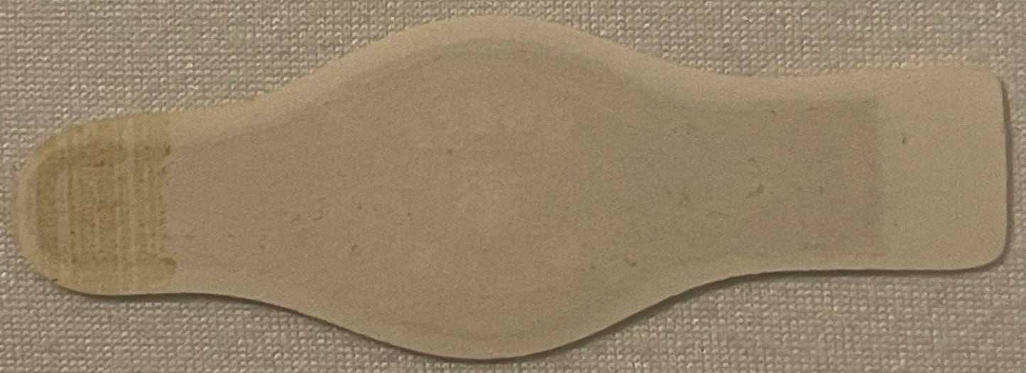 Cream-colored vintage cigar band with wavy edges laid flat on beige fabric, showing faint printed text on left side.