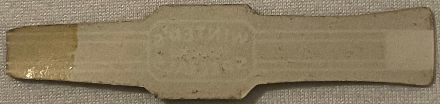 Cream-colored rectangular cigar band with decorative notched edges, displayed on textured fabric background