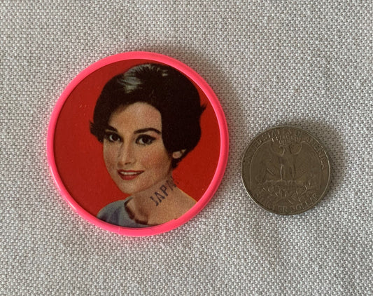 Vintage pocket mirror with bright pink plastic case featuring portrait of woman with dark hair on red background, shown next