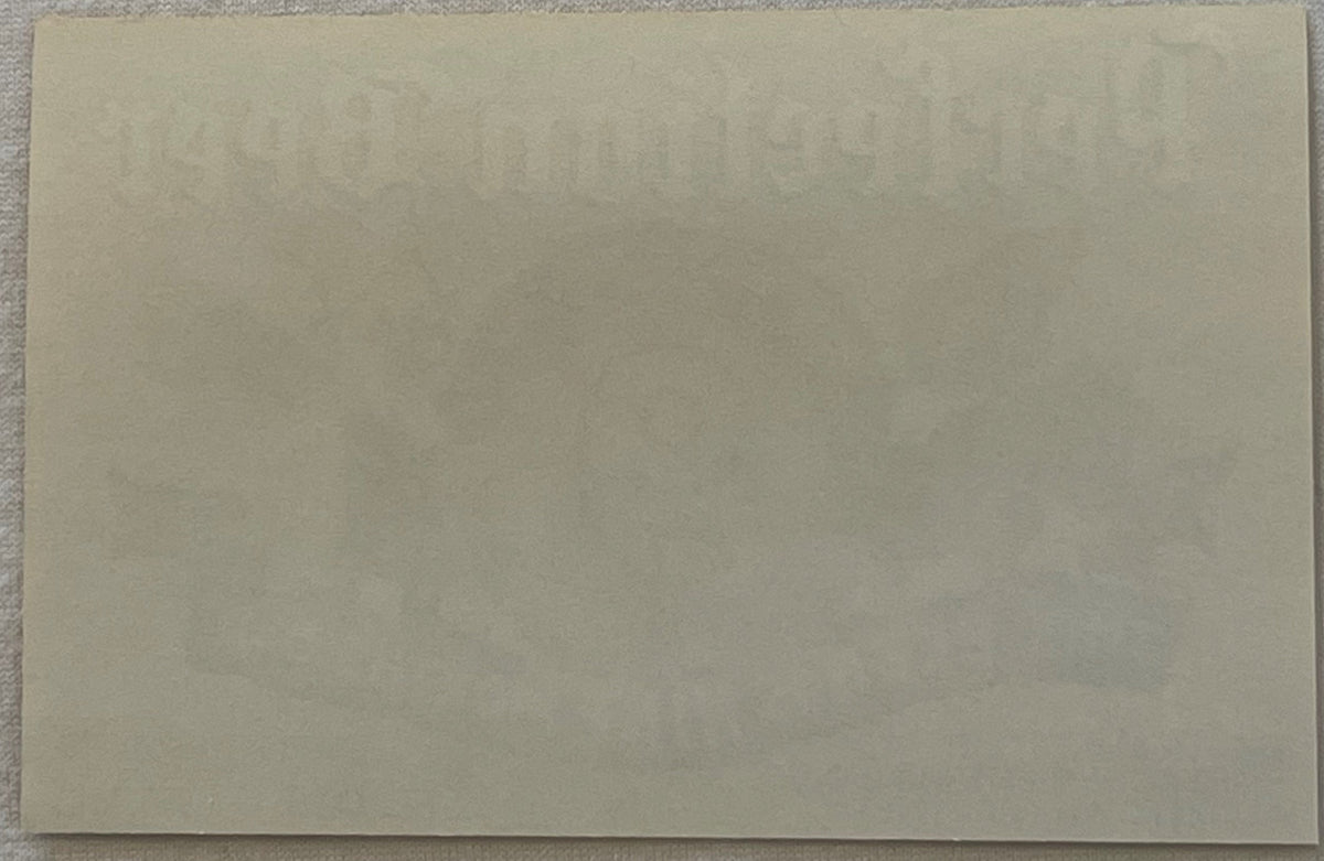 Blank cream-colored paper or label backing photographed flat against gray fabric surface