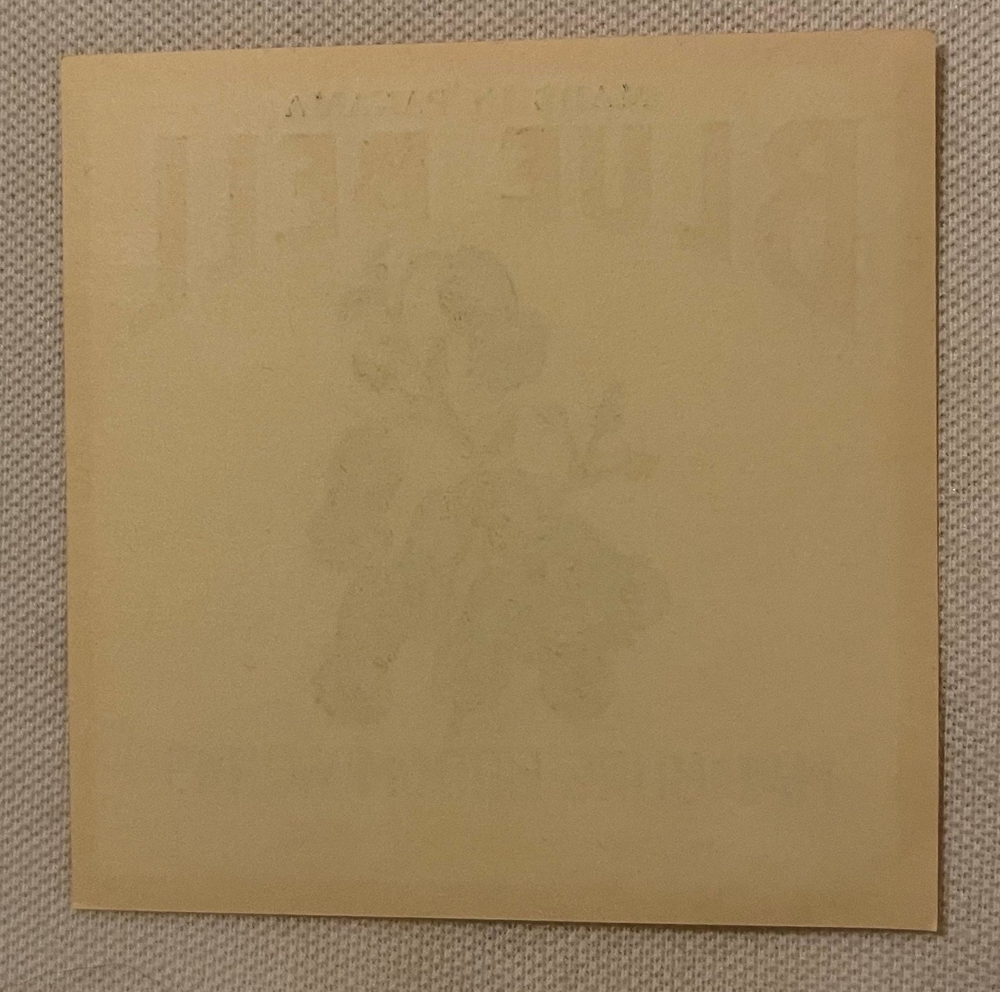 Blank tan cardboard sheet on textured beige fabric background, faint text visible at top edge