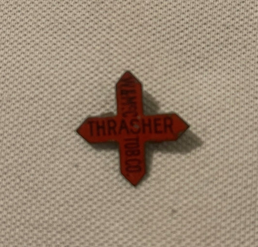Red die-cut cross-shaped tobacco tag with "THRASHER" embossed text, displayed on cream fabric background