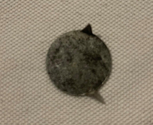Worn circular metal tobacco tin tag with embossed text, photographed against textured fabric background