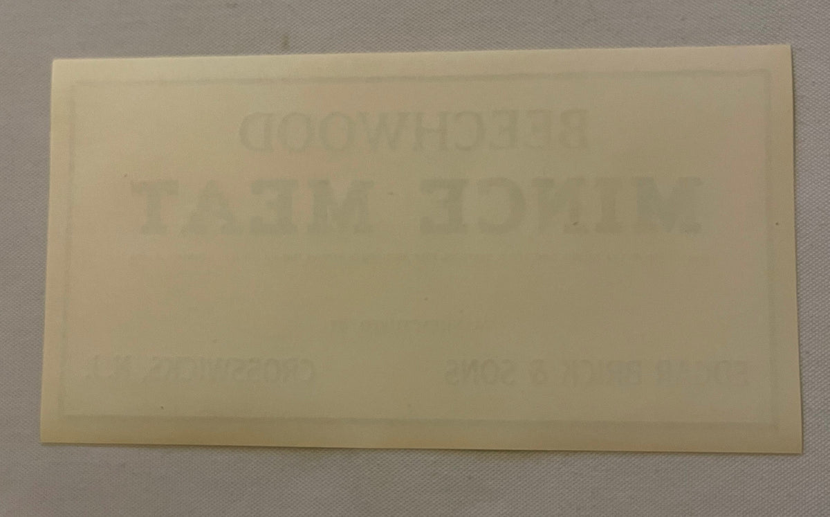 Cream-colored rectangular beechwood label with faint embossed text, photographed flat against light gray background