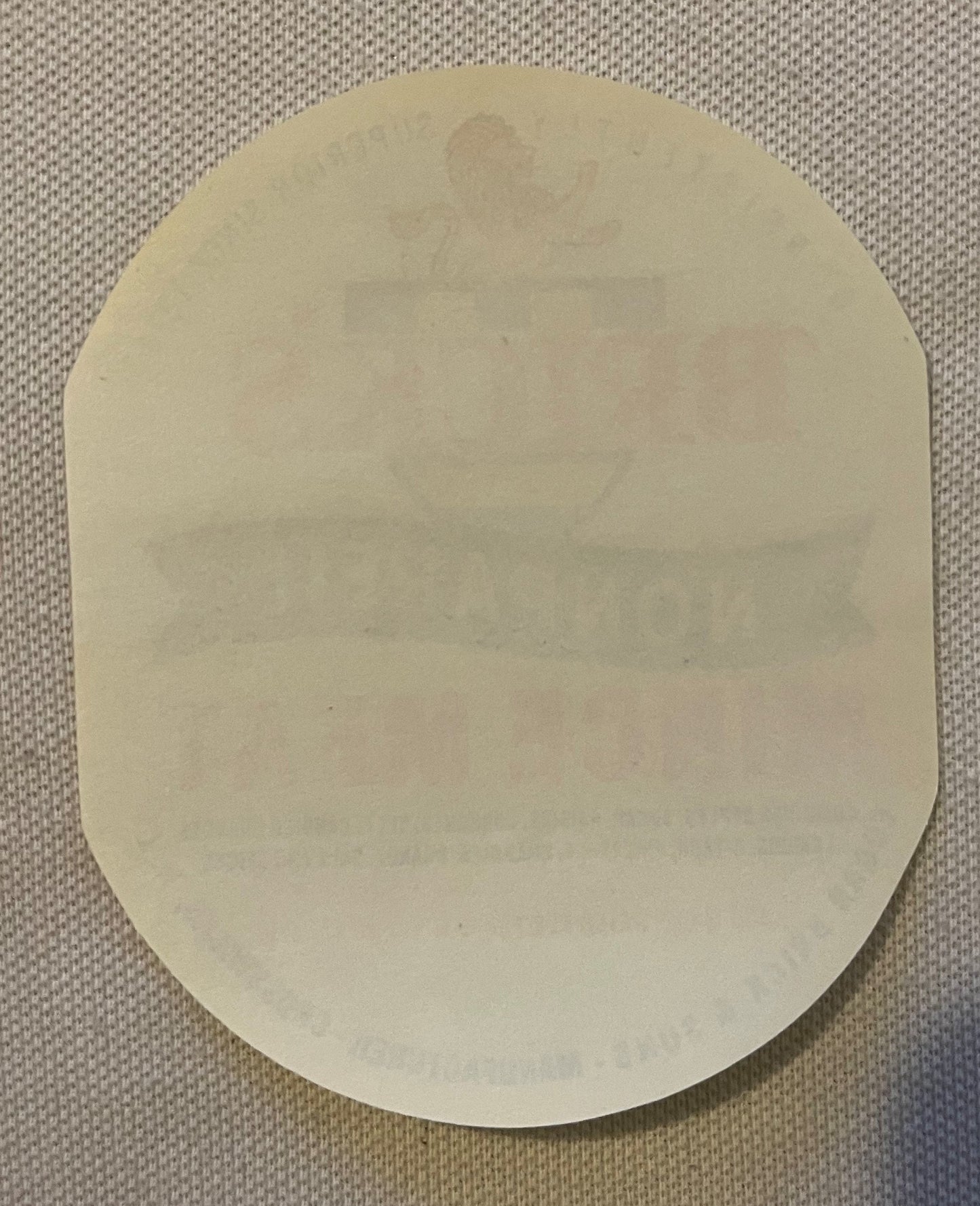 Cream-colored rounded rectangular label on textured beige fabric background, blank face visible