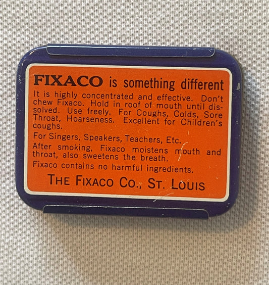 Vintage Fixaco throat confection tin with navy blue case and orange label against tan fabric background.