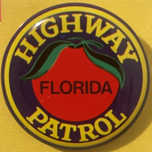 Circular tin litho badge pin with yellow border, dark purple center, red circle, green leaf detail, and yellow text reading "