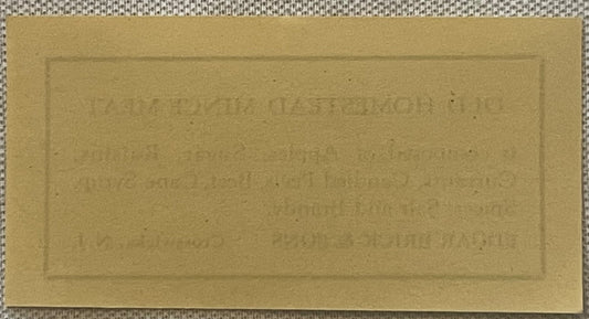 Tan paper strip label with embossed text for Brick's Old Homestead Mince Meat, displayed flat on textured fabric background
