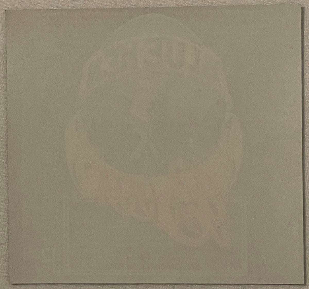 Blank cream-colored paper or backing against gray textured surface, no visible beer label or text