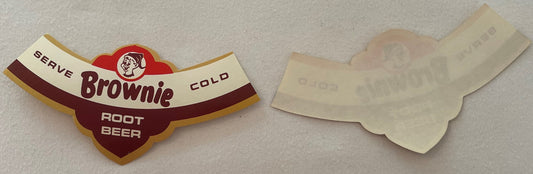 Vintage Brownie Root Beer neck label front and back showing red and cream design with elf mascot, laid flat on beige fabric.