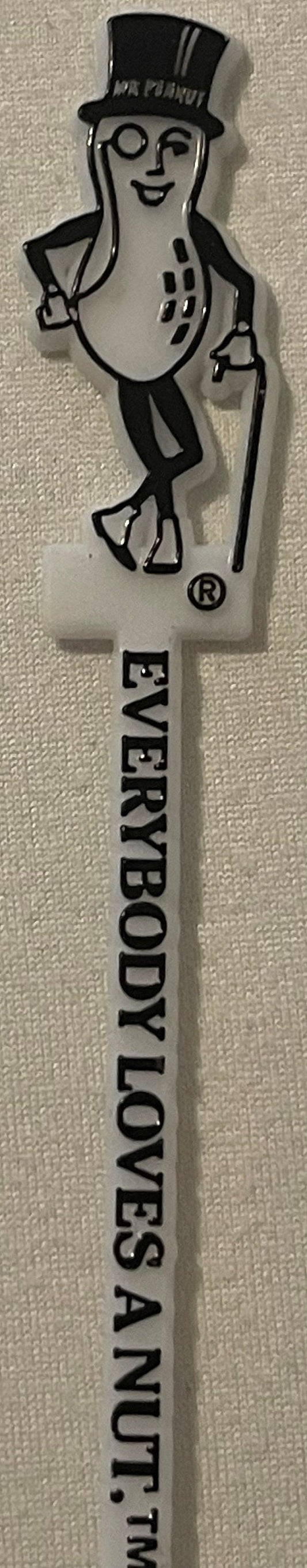 Vintage white plastic Mr. Peanut swizzle stick with black printed text reading "Everybody Loves a Nut" and trademark symbol,