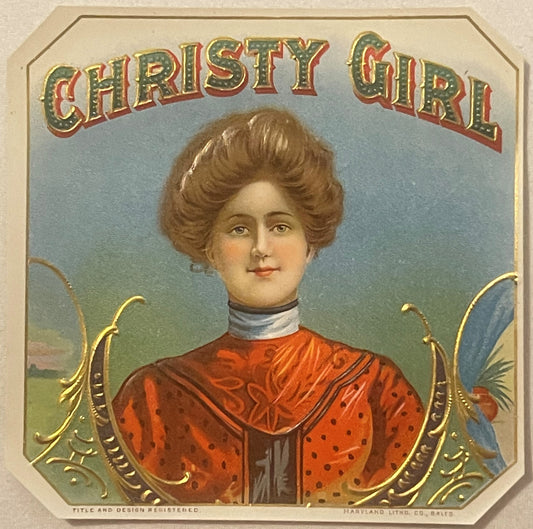 Vintage cigar label with "Christy Girl" text showing woman in red dress with brown hair against blue-green background, gold d